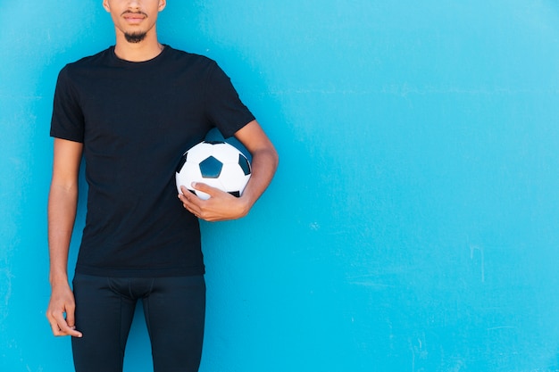 Crop of ethnic sportsman with soccer-ball under arm