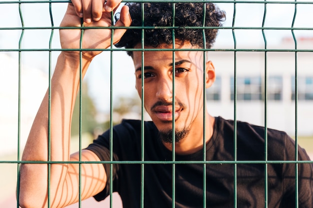 Free photo crop ethnic young man behind fence