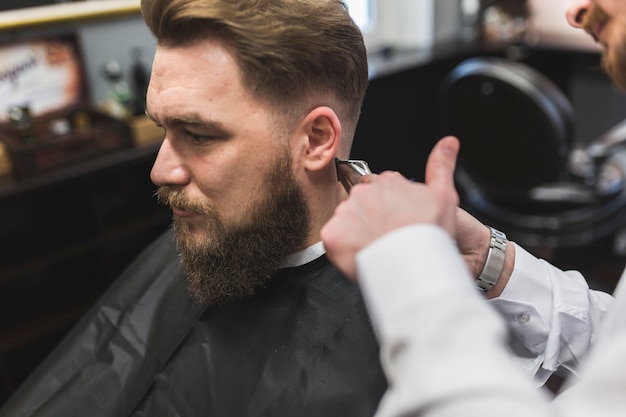 Crop hairdresser shaving hair of bearded man