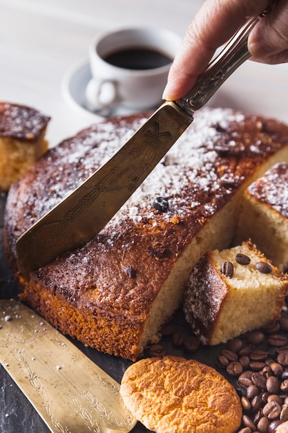 Crop hand cutting cake for coffee