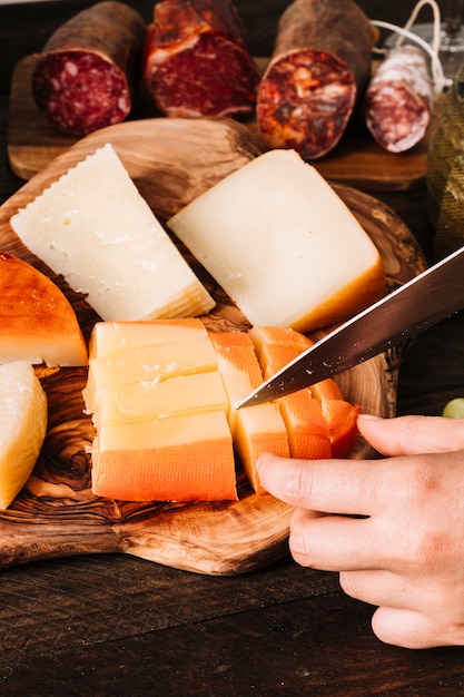 Free photo crop hand cutting cheese near sausages