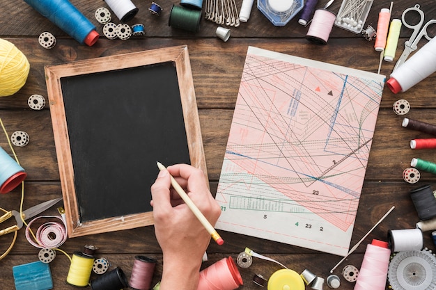 Crop hand drawing on blackboard near sewing stuff