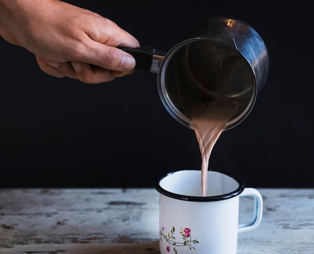 Crop hand filling cup with hot chocolate