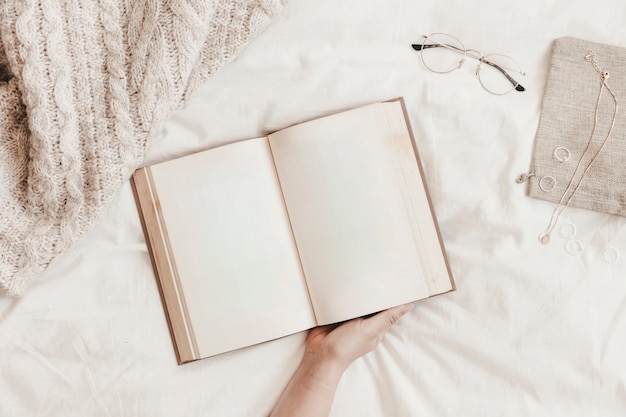 Free photo crop hand holding book near accessories on bed