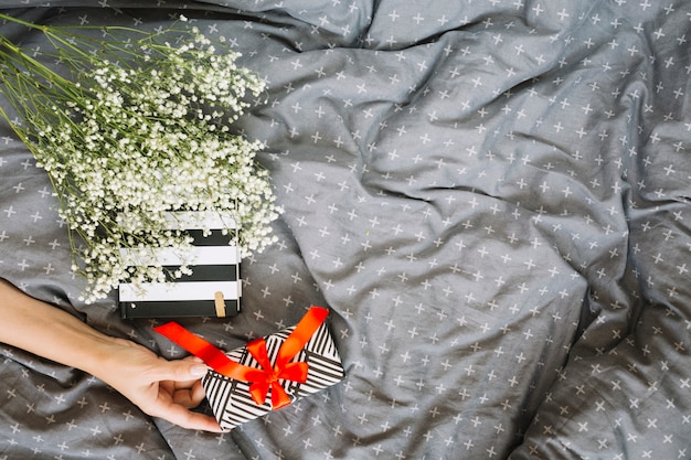 Crop hand holding gift near bouquet and notebook