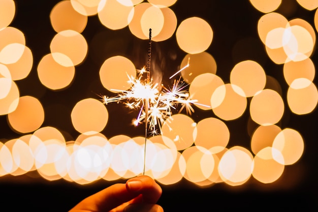 Free photo crop hand holding sparkler near lights