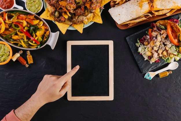 Crop hand pointing at blackboard near food