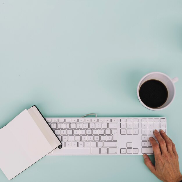 Crop hand using keyboard near notebook and coffee