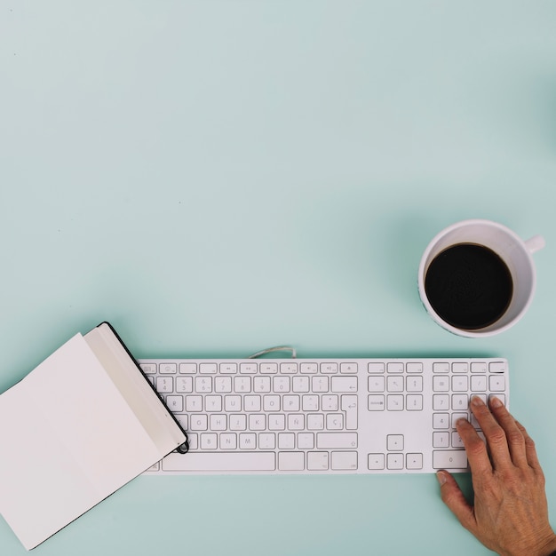 Crop hand using keyboard near notebook and coffee