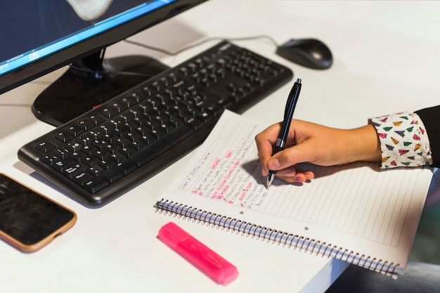 Crop hand writing in notebook near computer