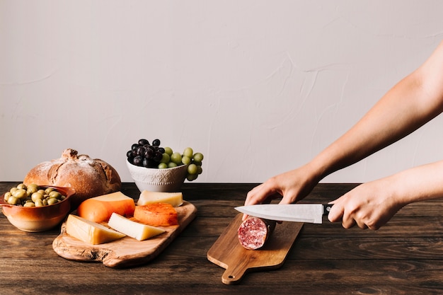 Free Photo crop hands cutting sausage near food