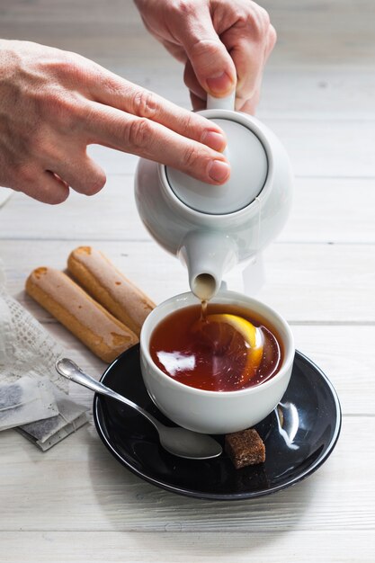 Crop hands filling cup with tea