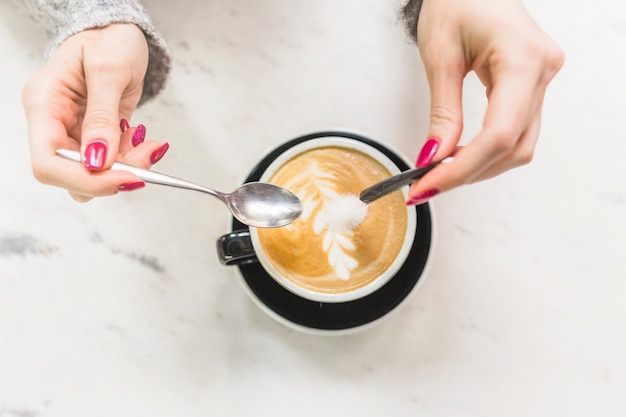 Free photo crop hands pouring sugar into cappuccino cup