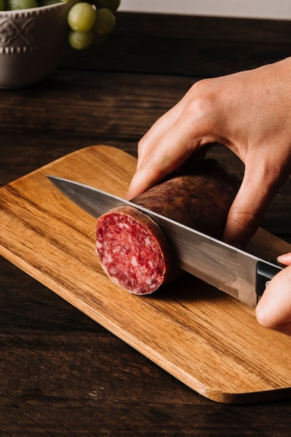 Free photo crop hands slicing smoked sausage on board