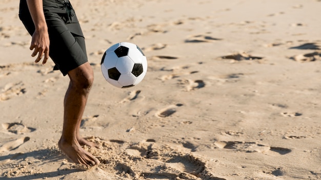 Free Photo crop man kicking ball on sandy beach