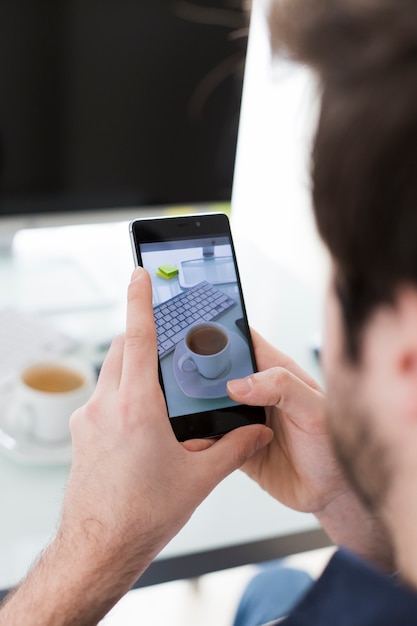 Crop man taking picture of cup in office