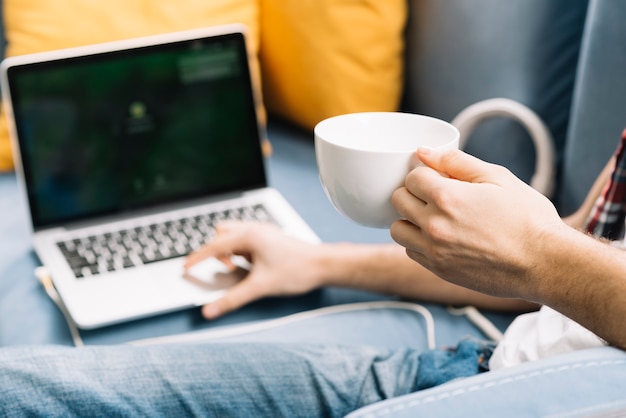 Free photo crop man with cup using laptop