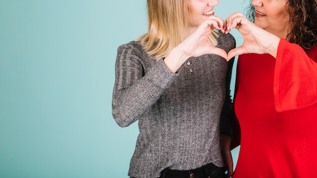 Crop mother and daughter making heart gesture