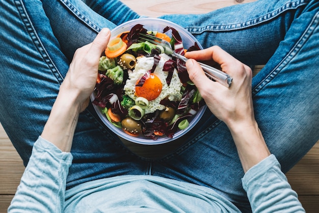 Crop person eating salad with fried egg