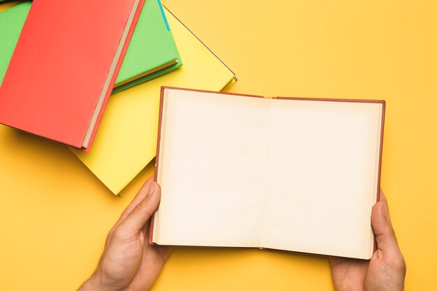 Crop person holding open notebook near stack of books