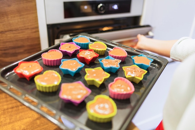 Crop person putting cupcakes into oven