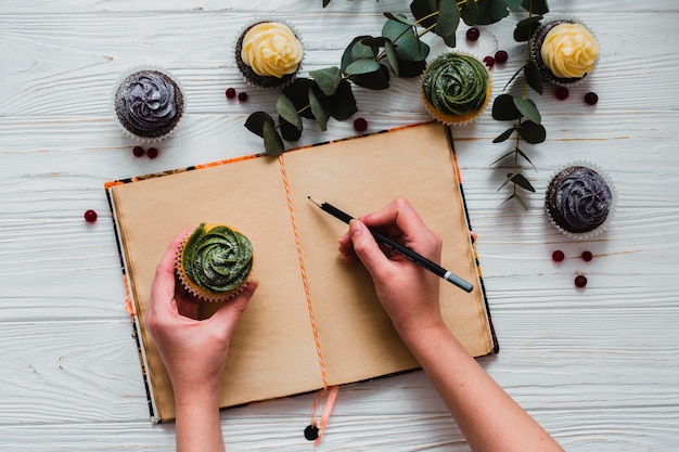 Free photo crop person with cupcake writing in notebook