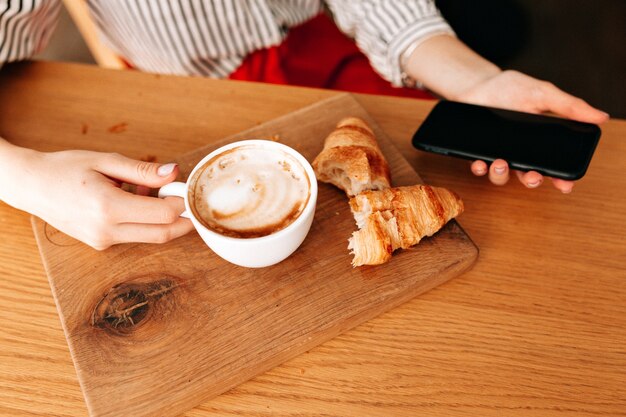 Crop photo of cup with coffee and french croissants ion the table on wood desk.