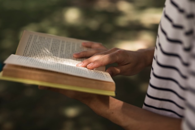 Crop student reading book in park