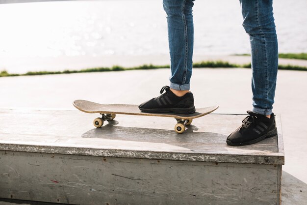 Crop teenager stepping on skateboard on border