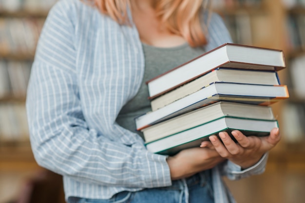 Crop teenager with heap of books