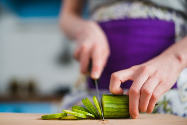 Crop woman chopping cucumber