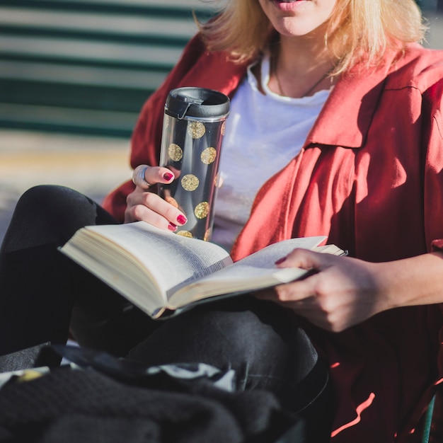 Crop woman enjoying book and drink