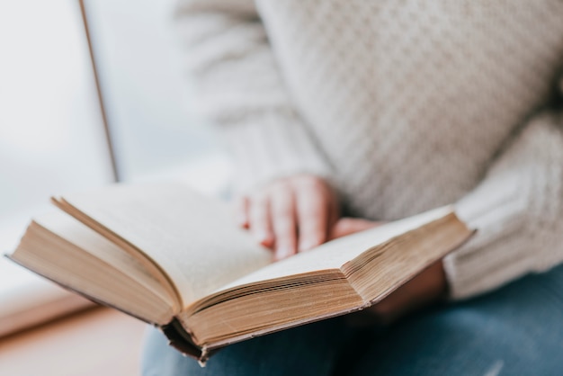 Free photo crop woman enjoying reading near window