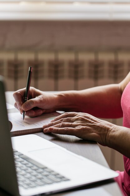 Crop woman near laptop making notes