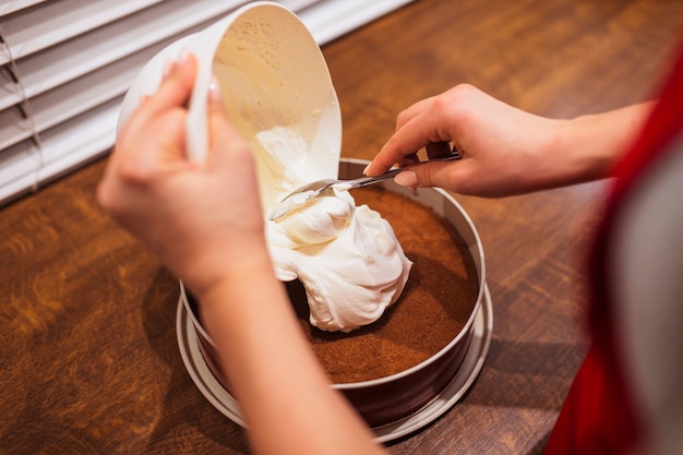 Crop woman putting cream on cake