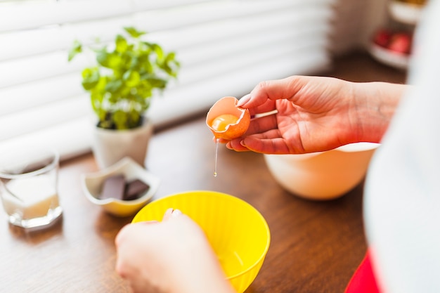 Free photo crop woman putting raw eggs into bowl