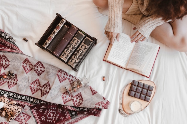 Crop woman reading book near chocolate