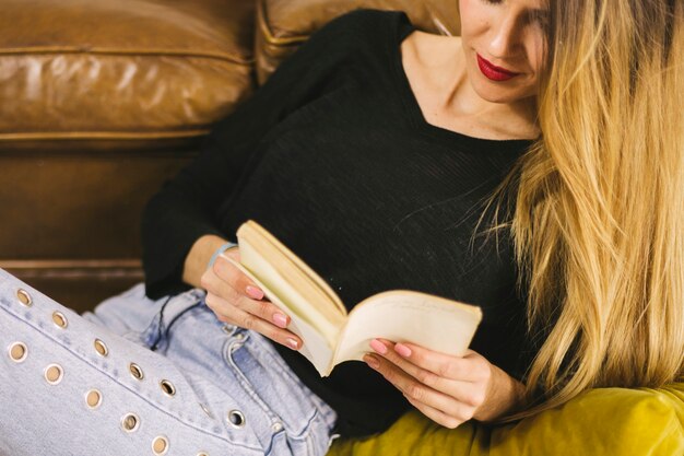 Crop woman reading book near sofa