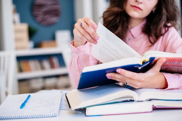 Crop woman reading textbooks in library