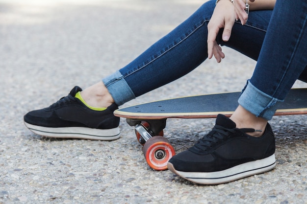 Free photo crop woman sitting on longboard