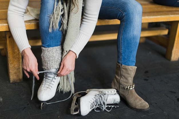 Crop woman tying laces on ice skates