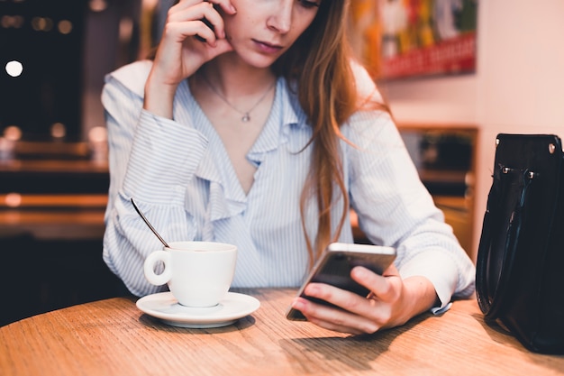 Crop woman using smartphone at cafe table