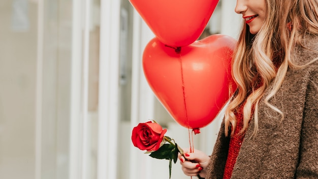 Crop woman with balloons and rose