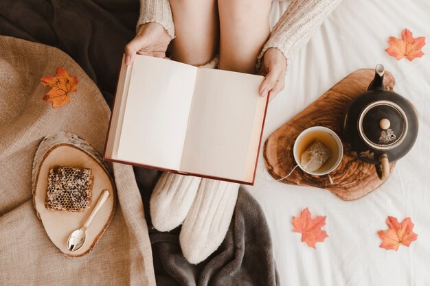 Crop woman with book near tea and honeycomb