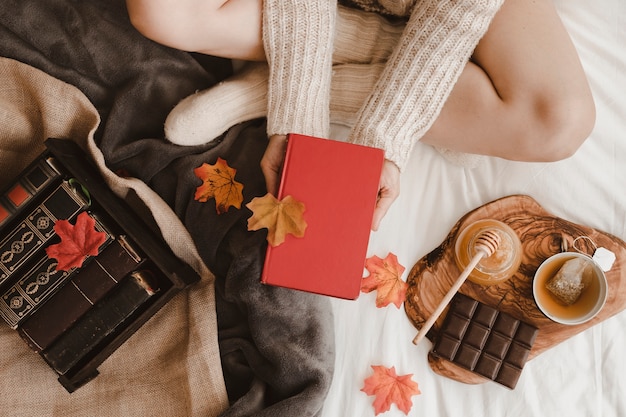 Free photo crop woman with book near tea and leaves