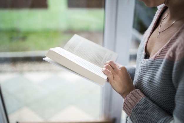 Crop woman with book near window