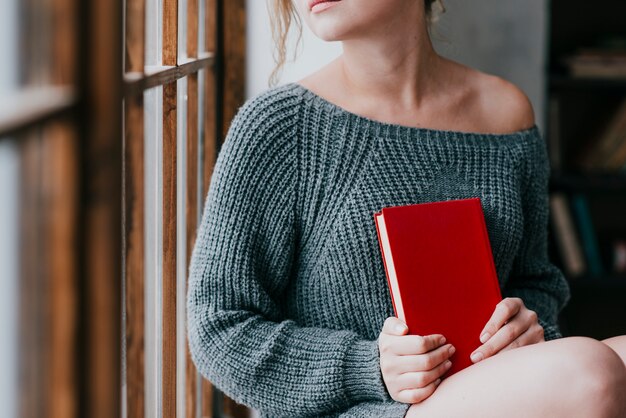 Crop woman with book sitting near window