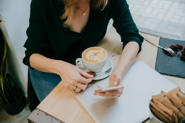 Crop woman with coffee using smartphone