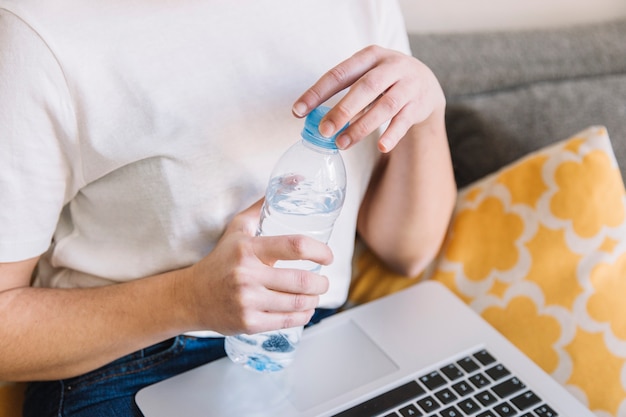 Free Photo crop woman with laptop opening water bottle