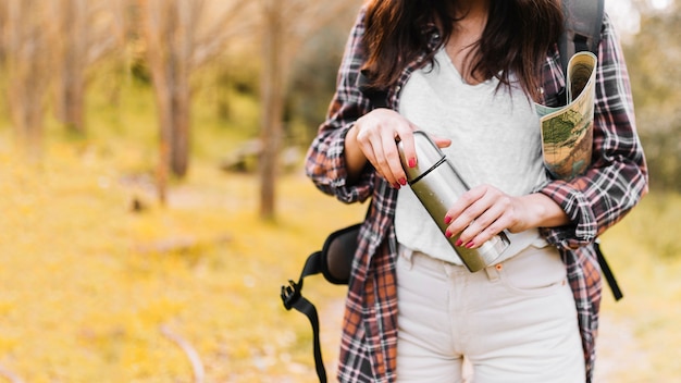 Crop woman with map closing thermos